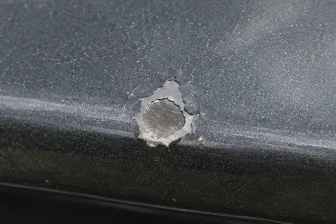 Steinschlag an der Vorderkante einer grauen Motorhaube, in der Mitte glänzt das blanke Blech.