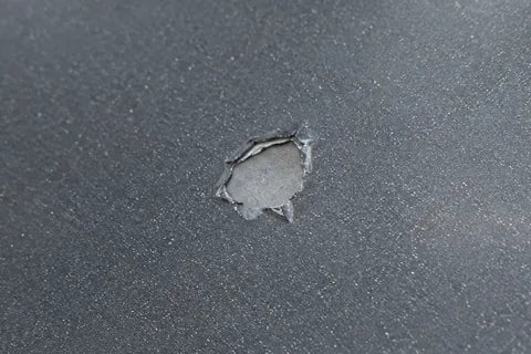 Kleiner Steinschlag auf einer grauen Motorhaube, in der Mitte ist die hellgraue Grundierung zu sehen.