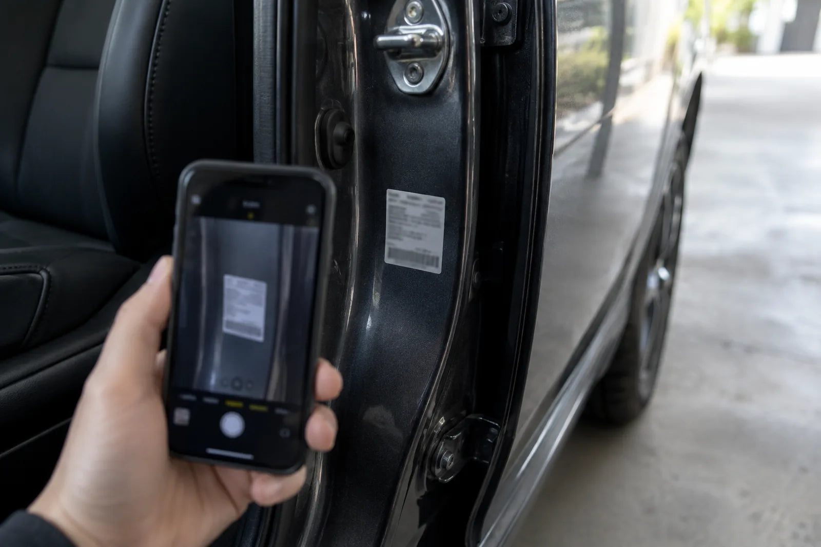 Eine Hand fotografiert mit dem Smartphone den Aufkleber mit dem Farbcode an der B-Säule eines Autos.